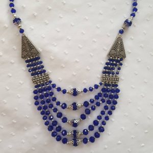 Bewitching Blue - Handmade Kalasha Necklace The Bewitching Blue necklace celebrates both style and elegance with traditional touch. Glistening blue Aqeeq stones are arranged in five layers giving it an intriguing look! This piece is perfect for formal and party wear, bound to make you feel like the lady of the night! Colour: Blue Stone: Aqeeq