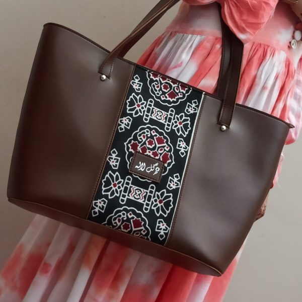 Brown Motif - Faux Leather Tote Bag A classical handbag with a traditional twist. Featuring a simple & popular silhouette, this bag is perfect to carry everything you need to have with you when on the go! Made out of faux leather with traditional printed fabric incorporated to make it stand out and give it a desi touch!