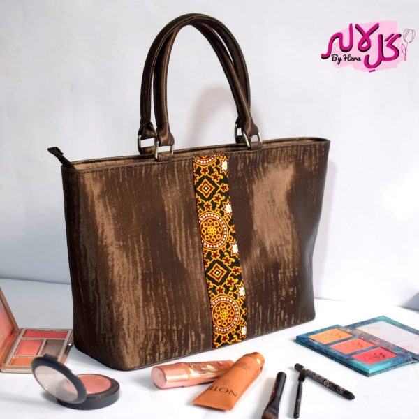 The Chocolate Glow - Faux Leather Hand Bag A shiny beautiful handbag with a traditional twist. Featuring a simple & popular silhouette, this bag is perfect to carry everything you need to have with you when on the go! Made out of faux leather with traditional printed fabric incorporated to make it stand out and give it a desi touch! Colour: Brown