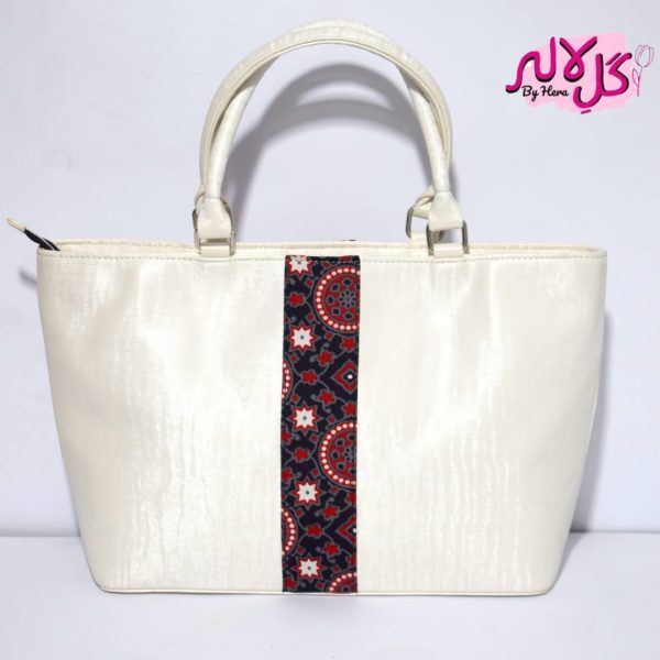 White Shimmer - Faux Leather Hand Bag A shiny beautiful handbag with a traditional twist. Featuring a simple & popular silhouette, this bag is perfect to carry everything you need to have with you when on the go! Made out of faux leather with traditional printed fabric incorporated to make it stand out and give it a desi touch!